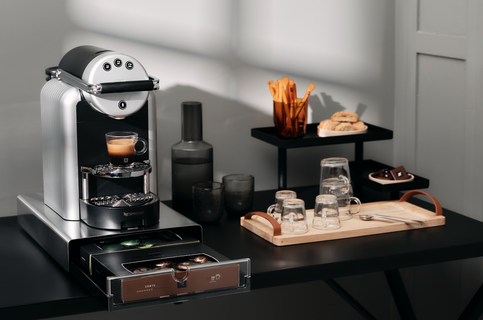 A Nespresso Zenius coffee machine making a coffee next to glasses and snacks.