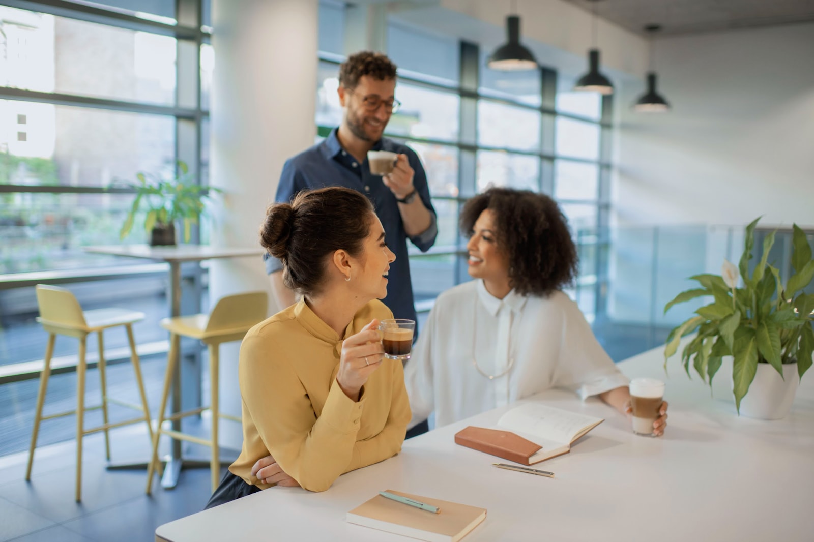 Three employees chatting and drinking coffee in an open plan office.