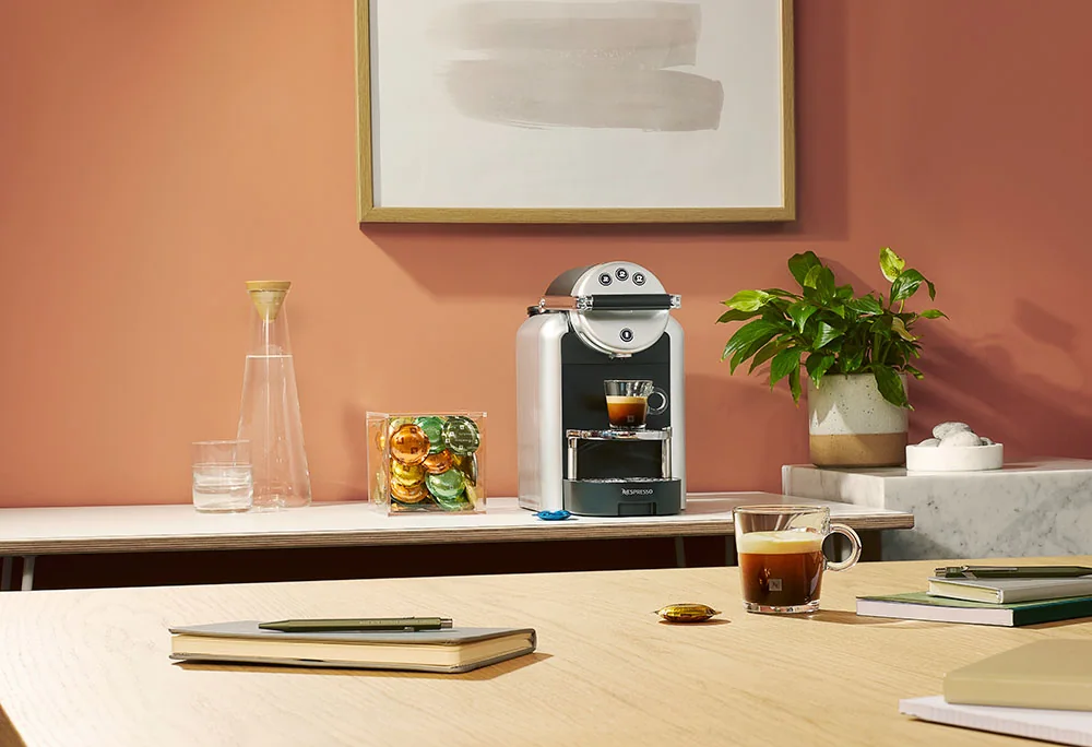 Nespresso Zenius machine set up in a warm office meeting room with coffee, capsules and desk accessories